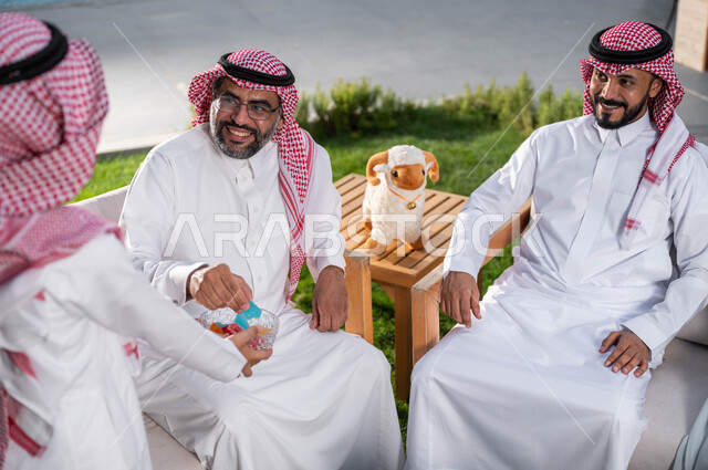 قضاء اوقات ممتعة مع  الابناء في الشاليهات والمنتجعات في ايام العيد السعيد في السعوديه, فتى عربي خليجي سعودي يرتدي الزي التقليدي السعودي ويقوم بتقديم توزيعات عيد الاضحى المبارك,  التجمعات والزيارات الاسرية, أعياد ومناسبات اسلامية, ايماءات تدل على السعاده 