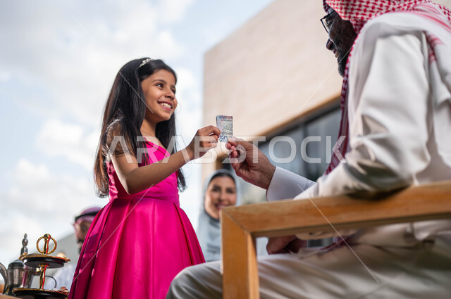 أعياد ومناسبات اسلامية, تقديم العيدية للأطفال , ايماءات تدل على السعاده , رجل مسن عربي خليجي سعودي يحتفل في العيد  مع الابناء و الاحفاد  في الشاليهات والمنتجعات في ايام العيد السعيد في السعوديه, التجمعات والزيارات الاسرية