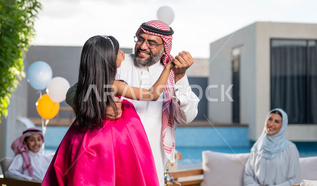 انشطه ترفيهيه في الاعياد  والمناسبات العائليه, رجل كبير السن عربي خليجي سعودي يرتدي الزي التقليدي السعودي يقوم باللعب مع حفيدته في احدى الشاليهات الفاخره ، اجتماع العائله والاحتفال مع الأطفال في العيد السعيد 