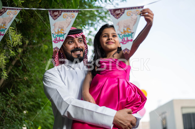 ديكورات وزينة العيد السعيد,  قضاء أوقات ممتعة مع الابناء  في الشاليهات والمنتجعات في ايام العيد السعيد في السعوديه, صورة مقربة لأب عربي خليجي سعودي يحمل ابنته ويحتفلون في العيد الاضحى,  ايماءات تدل على الفرح والسعاده, مناسبات وأعياد اسلامية .