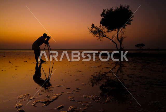 خلفية طبيعة، صورة ابداعية لمشهد الغروب على شواطئ البحر الأحمر في المملكة العربية السعودية، جمال الطبيعة الخلابة والأمواج الهادئة في جزيرة فرسان جيزان ، صورة ظلية لشخص يقوم بتصوير شاطئ البحر