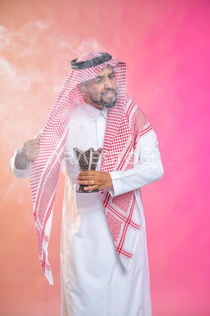 استخدام خشب العود في المناسبات والأعياد, التطيب بالبخور والعود، بورتريه لرجل عربي سعودي خليجي يرتدي الثوب و الشماغ السعودي التقليدي يتعطربحامل البخور ( المبخرة ) ، العادات والتقاليد السعودية, خلفية ملونة.