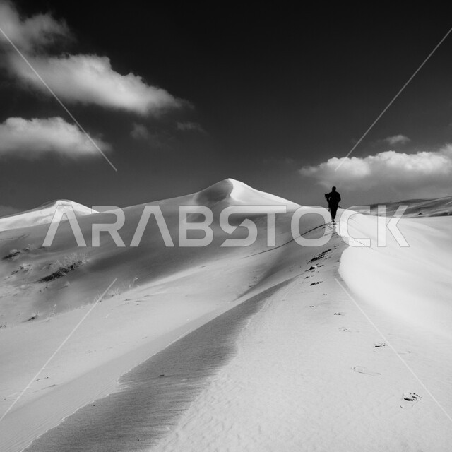 صورة ضبابية بالابيض والأسود لرجل يقف على التلال والكثبان الرملية في صحراء المملكة العربية السعودية ، الرمال الذهبية الناعمةو التضاريس الصحراوية في شبه الجزيرة العربية 
