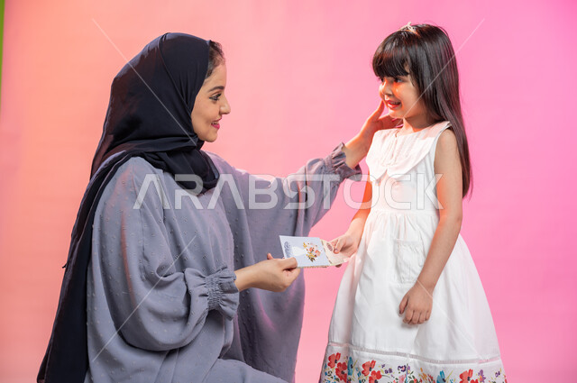  إيماءات تدل على الفرح والسرور بالعيد السعيد , بورتريه لإمرأة عربية سعودية خليجية محجبة ترتدي العباءة تقوم بتقديم العيدية لطفلة صغيرة ، مناسبات واعياد اسلاميه, خلفية ملونة.