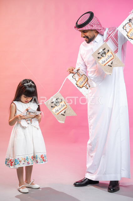 الاحتفالات العائلية بالأعياد الاسلامية المباركة و المناسبات ، , بورتريه لرجل يرتدي الثوب و الشماغ السعودي التقليدي مع ابنته يقومون بالتحضير و التزيين لاستقبال الأعياد السعيدة ، التجمعات الأسرية في العيد ، زينة العيد ، صورة الجسم بالطول الكامل, خلفية ملونة