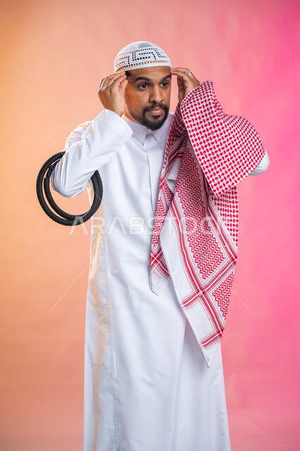التزين و التجمل و الترتيب, الاهتمام بالمظهر الخارجي و الشياكه و  الأناقة, شاب سعودي عربي خليجي يرتدي الثوب و الشماغ الأحمر, الاستعداد للخروج, خطوات لبس الشماغ السعودي التقليدي, خلفية ملونة.