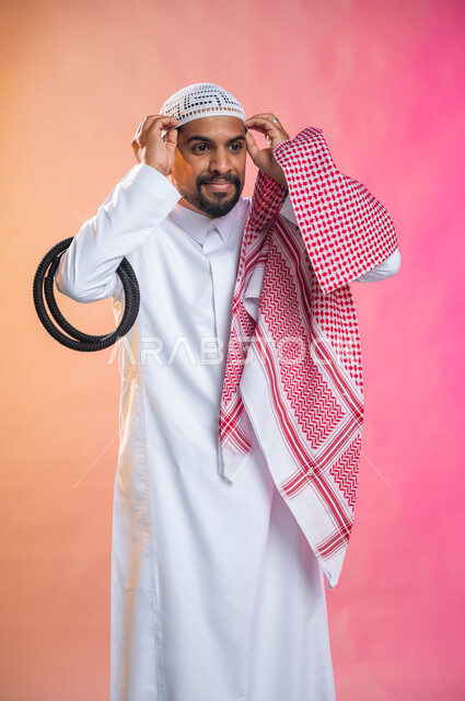التزين و التجمل و الترتيب, الاهتمام بالمظهر الخارجي و الشياكه و  الأناقة, شاب سعودي عربي خليجي يرتدي الثوب و الشماغ الأحمر, الاستعداد للخروج, خطوات لبس الشماغ السعودي التقليدي, خلفية ملونة.