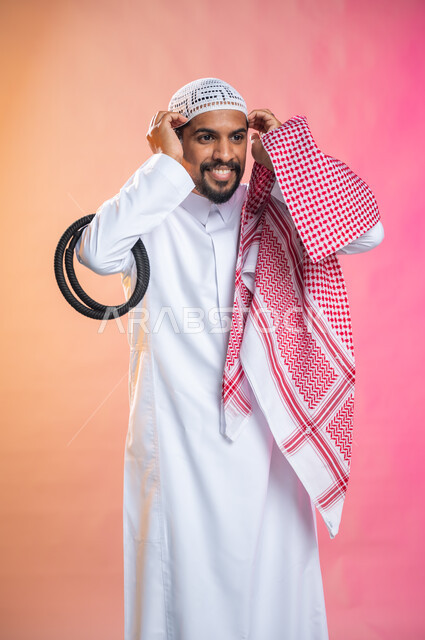 التزين و التجمل و الترتيب, الاهتمام بالمظهر الخارجي و الشياكه و  الأناقة, شاب سعودي عربي خليجي يرتدي الثوب و الشماغ الأحمر, الاستعداد للخروج, خطوات لبس الشماغ السعودي التقليدي, خلفية ملونة.