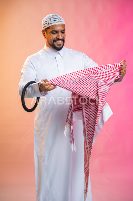 التزين و التجمل و الترتيب, الاهتمام بالمظهر الخارجي و الشياكه و  الأناقة, شاب سعودي عربي خليجي يرتدي الثوب و الشماغ الأحمر, الاستعداد للخروج, خطوات لبس الشماغ السعودي التقليدي, خلفية ملونة.