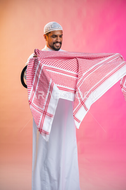 التزين و التجمل و الترتيب, الاهتمام بالمظهر الخارجي و الشياكه و  الأناقة, شاب سعودي عربي خليجي يرتدي الثوب و الشماغ الأحمر, الاستعداد للخروج, خطوات لبس الشماغ السعودي التقليدي, خلفية ملونة.