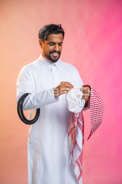 الاستعداد للخروج, التزين و التجمل و الترتيب, شاب سعودي عربي خليجي يرتدي الثوب و الشماغ الأحمر, الاهتمام بالمظهر الخارجي و الشياكه و  الأناقة, خطوات لبس الشماغ السعودي التقليدي, خلفية ملونة.