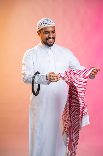 الاستعداد للخروج, التزين و التجمل و الترتيب, شاب سعودي عربي خليجي يرتدي الثوب و الشماغ الأحمر, الاهتمام بالمظهر الخارجي و الشياكه و  الأناقة, خطوات لبس الشماغ السعودي التقليدي, خلفية ملونة.