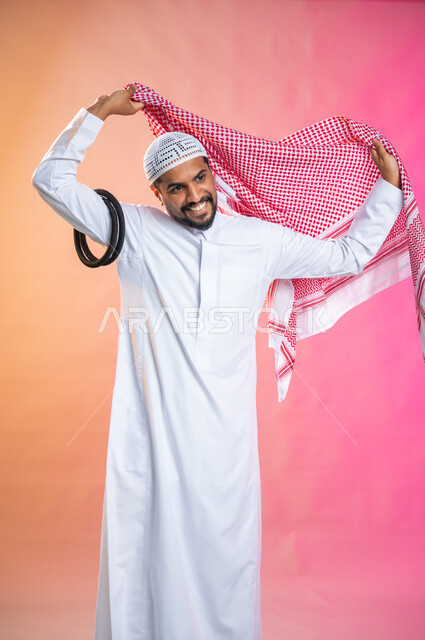 الاستعداد للخروج, التزين و التجمل و الترتيب, شاب سعودي عربي خليجي يرتدي الثوب و الشماغ الأحمر, الاهتمام بالمظهر الخارجي و الشياكه و  الأناقة, خطوات لبس الشماغ السعودي التقليدي, خلفية ملونة.