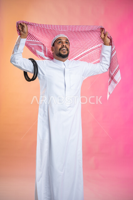 Steps to wear the traditional Saudi shemagh,  Getting ready to go out, adorning, beautifying and arranging, a young Saudi Arab Gulf man wearing a red dress and shemagh, taking care of the external appearance, elegance and elegance, a colored background.