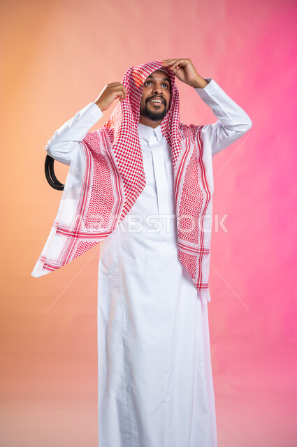 خطوات لبس الشماغ السعودي التقليدي,   الاستعداد للخروج, التزين و التجمل و الترتيب, شاب سعودي عربي خليجي يرتدي الثوب و الشماغ الأحمر, الاهتمام بالمظهر الخارجي و الشياكه و  الأناقة, خلفية ملونة.