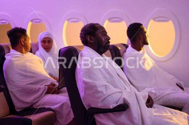 آداء العمرة في رمضان، مجموعة من حجاج الخارج يجلسون في مقصورة الطائرة ويرتدون ملابس الاحرام، موسم الحج 2023، السفر الى مكة لآداء مناسك الحج والعمرة، استقبال الحجاج من خارج السعودية، خطوط الطيران السعودي