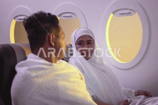 السفر الى مكة لآداء مناسك الحج والعمرة، آداء العمرة في رمضان، الاستعداد للذهاب للحج، زوجان اندونيسيان ملسمان يرتديان ملابس الاحرام ويجلسان في الطائرة، موسم الحج 2023، خطوط الطيران السعودي