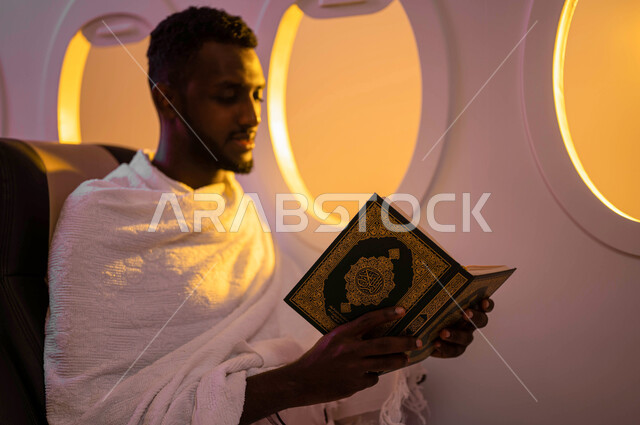 ارتداء ملابس الاحرام، السفر الى مكة لآداء مناسك الحج والعمرة، رجل عربي سوداني يقوم بقراءة وتلاوة القران، الجلوس في مقعد الطائرة، حفظ وتفسير القران الكريم، موسم الحج 2023، آداء العمرة في رمضان، خطوط الطيران السعودي