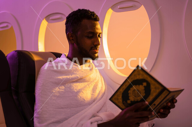 رجل عربي سوداني يقوم بقراءة وتلاوة القران، الجلوس في مقعد الطائرة، حفظ وتفسير القران الكريم، ارتداء ملابس الاحرام، السفر الى مكة لاداء مناسك الحج والعمرة، موسم الحج 2023، آداء العمرة في رمضان، خطوط الطيران السعودي