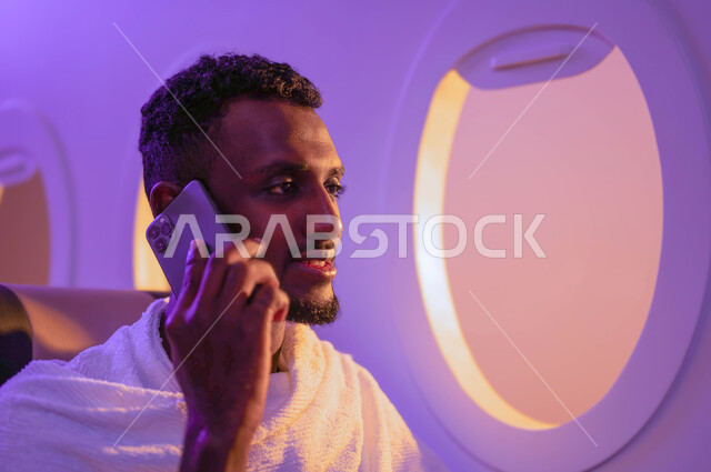 التواصل والدردشة مع الافرد، رجل عربي سوداني يجلس في الطائرة ويستخدم الهاتف المحمول، اجراء مكالمة هاتفية، ارتداء ملابس الاحرام، السفر الى مكة لآداء مناسك الحج والعمرة، موسم الحج 2023، فضل العمرة في رمضان، خطوط الطيران السعودي