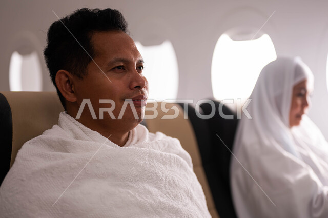 السفر الى مكة لآداء مناسك الحج والعمرة، الاستعداد للذهاب للحج، زوجان اندونيسيان ملسمان يرتديان ملابس الاحرام ويجلسان في الطائرة، موسم الحج 2023، فضل العمرة في شهر رمضان، خطوط الطيران السعودي