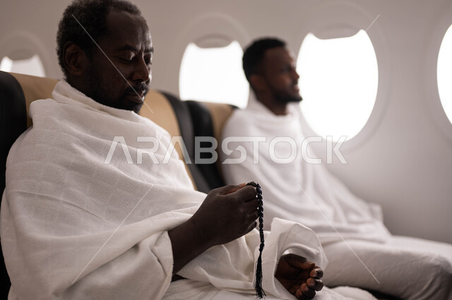 العباده والتقرب الى الله، التسبيح والاستغفار وذكر الله تعالى، رجلان عربيان من السودان يرتديان ملابس الاحرام ويجلسان في الطائرة، السفر الى مكة لآداء مناسك الحج والعمرة، موسم الحج 2023، آداء العمرة في رمضان، خطوط الطيران السعودي