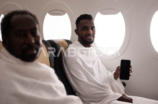 الهاتف المحمول بشاشة سوداء فارغة، الحجز الالكتروني لحملات الحج والعمرة باستخدام الجوال، رجلان عربيان من السودان يرتديان ملابس الاحرام ويجلسان في الطائرة، موسم الحج 2023، فضل العمرة في شهر رمضان، السفر الى مكة لآداء مناسك الحج والعمرة، خطوط الطيران السعودي