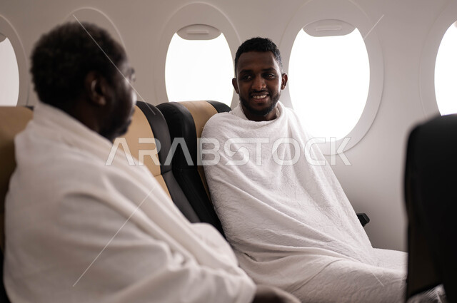 رجلان عربيان من السودان يرتديان ملابس الاحرام ويجلسان في مقعد الطائرة، السفر الى مكة لآداء مناسك الحج والعمرة، فضل العمرة في شهر رمضان، موسم الحج 2023، آداء العمرة في رمضان، خطوط الطيران السعودي