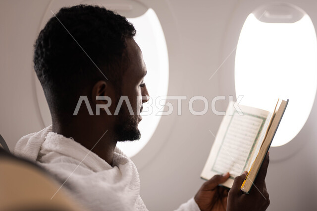 حفظ وتفسير القران الكريم، شاب سوداني مسلم اسمر البشرة يرتدي ملابس الاحرام ويقوم بقراءة وتلاوة القران، الجلوس في مقعد الطائرة، السفر الى مكة لآداء مناسك الحج والعمرة، موسم الحج 2023، آداء العمرة في رمضان، خطوط الطيران السعودي