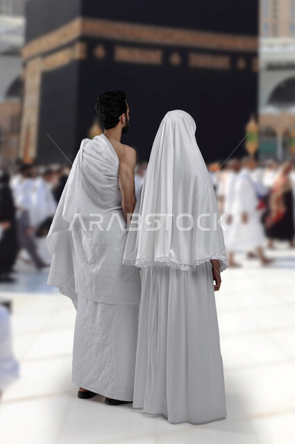 العمرة في شهر رمضان المبارك, اداء مناسك الحج والعمره في موسم الحج 2023،  صوره من الخلف لزوجان عربيان خليحيان سعوديان يرتديان ثياب الاحرام،  الركن الخامس من اركان الاسلام، اسلاميات وعباده, صورة الجسم بالطول الكامل, خلفية الكعبه المشرفه.