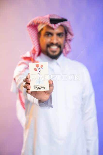 بهجه وفرحة استقبال العيد، بورتريه لرجل خليجي سعودي عربي يرتدي الثوب السعودي التقليدي والشماغ يمسك بيده بطاقة معايدة، الاحتفال بالأعياد والمناسبات الإسلامية السعيدة، خلفية ملونة، بطاقات تهنئة بعيد الأضحى، ايماءات تدل على الفرح والسرور 