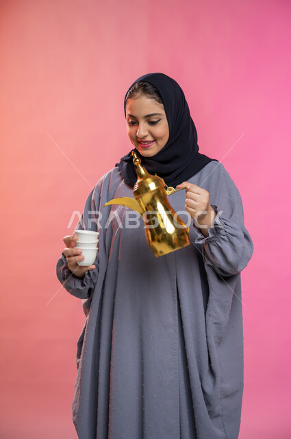 تقديم القهوة العربية في الأعياد والمناسبات ، بورتريه لسيدة عربية سعودية خليجية محجبة ترتدي العباءه الخليجية تقوم بصب فنجان قهوة ساخن، حسن الضيافة والاستقبال وإكرام الضيوف، خلفية ملونة