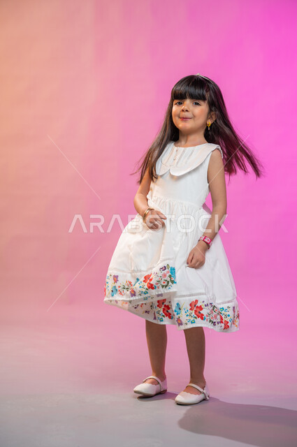 إيماءات تدل على الفرح والحماس والبهجة، بورتريه لطفلة عربية سعودية خليجية ترتدي فستان جميل تقفز فرحا وسعادة، صورة الجسم بالطول الكامل، خلفية ملونة