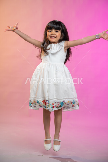Gestures indicating joy, enthusiasm and delight, a portrait of a Saudi Arabian Gulf girl wearing a beautiful dress jumping with joy and happiness, full-length body image, colored background