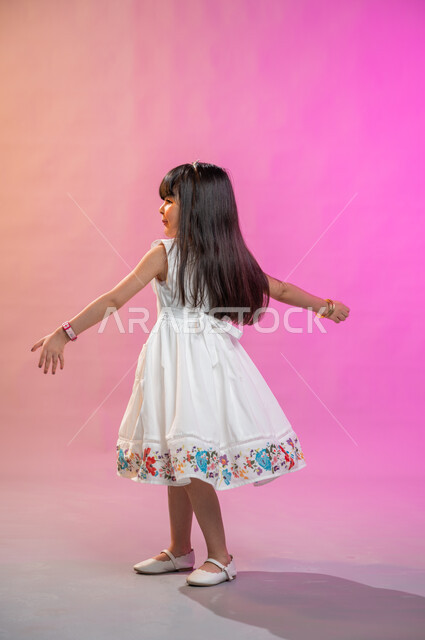 إيماءات تدل على الفرح والحماس والبهجة، بورتريه لطفلة عربية سعودية خليجية ترتدي فستان جميل تقفز فرحا وسعادة، صورة الجسم بالطول الكامل، خلفية ملونة