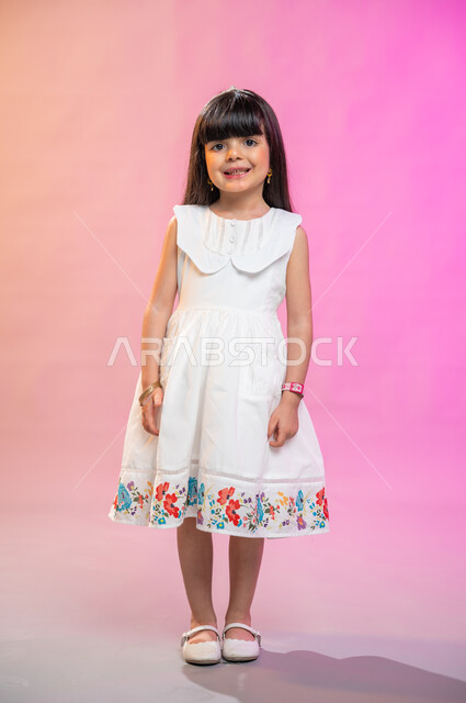  إيماءات وجه تدل على الفرح والبهجة والسرور، فرحة الأطفال بثياب العيد الجديدة ، بورتريه لطفلة عربية سعودية خليجية ترتدي فستان جميل، صورة الجسم بالطول الكامل، خلفية ملونة
