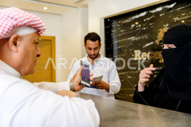 رجل عربي خليجي سعودي عند الاستقبال الخاص بالمستشفى ، يقوم بتعبئه بياناته عند موظفة الاستقبال ، استكمال اجراءات الدخول الى المستشفى ، تقديم الرعاية الصحية