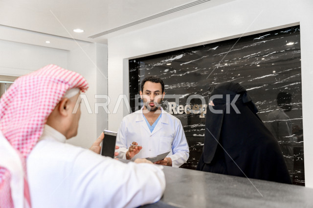 رجل عربي خليجي سعودي عند الاستقبال الخاص بالمستشفى ، يقوم بتعبئه بياناته عند موظفة الاستقبال ، استكمال اجراءات الدخول الى المستشفى ، تقديم الرعاية الصحية