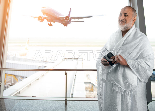 Facial gestures indicating happiness and enthusiasm for visiting the Sacred House of God, a Saudi Arabian Gulf man wearing Ihram clothes and holding a passport and plane ticket in his hand, preparing to go and set off for Makkah Al-Mukarramah, performing
