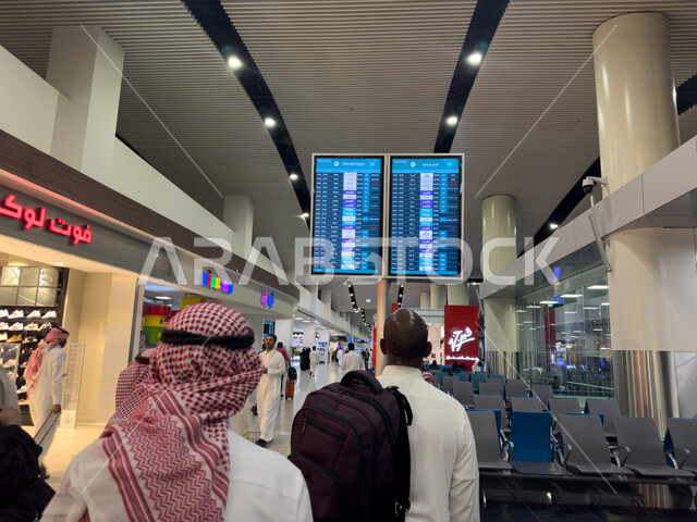 مجموعة من المسافرين العرب الخليجيين السعوديين يقفون امام شاشة الكترونية ارشادية، تحديد ومعرفة موعد الرحلات، مطار الملك عبد العزيز الدولي في المملكة العربية السعودية، رحلات جوية سياحية