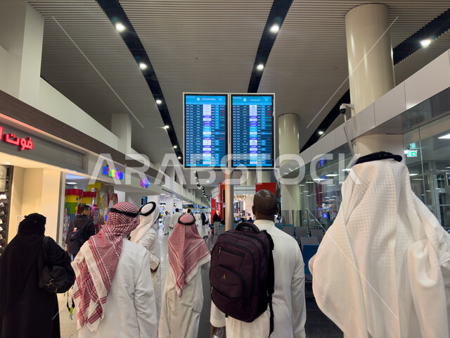 مجموعة من المسافرين العرب الخليجيين السعوديين يقفون امام شاشة الكترونية ارشادية، تحديد ومعرفة موعد الرحلات، مطار الملك عبد العزيز الدولي في المملكة العربية السعودية، رحلات جوية سياحية
