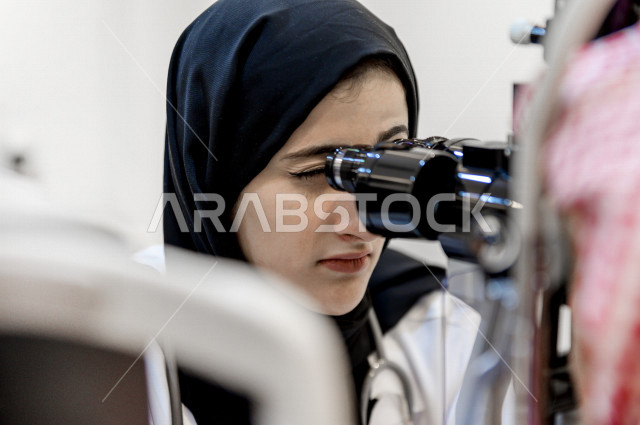 A Saudi Gulf Arab man in a specialized clinic for eye examination looks through a set of lenses, a Saudi Gulf doctor performs a set of tests to assess vision and detect eye diseases for the patient, providing services and health care