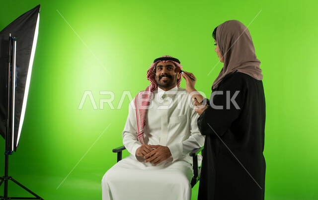 امرأة عربية سعودية خليجية تقوم بتحضير وتجميل العارض للصور الفوتوغرافية، كروما لجلسة تصوير في الاستوديو، الاستعداد لجلسة التصوير، خلفية شاشة خضراء، خلف الكواليس