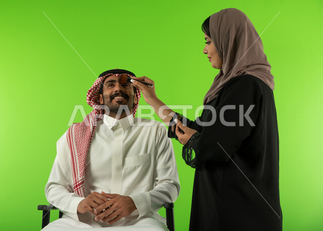 الاستعداد لجلسة التصوير، امرأة عربية سعودية خليجية تقوم بتحضير وتجميل العارض للصور الفوتوغرافية، كروما لجلسة تصوير في الاستوديو، خلفية شاشة خضراء، خلف الكواليس