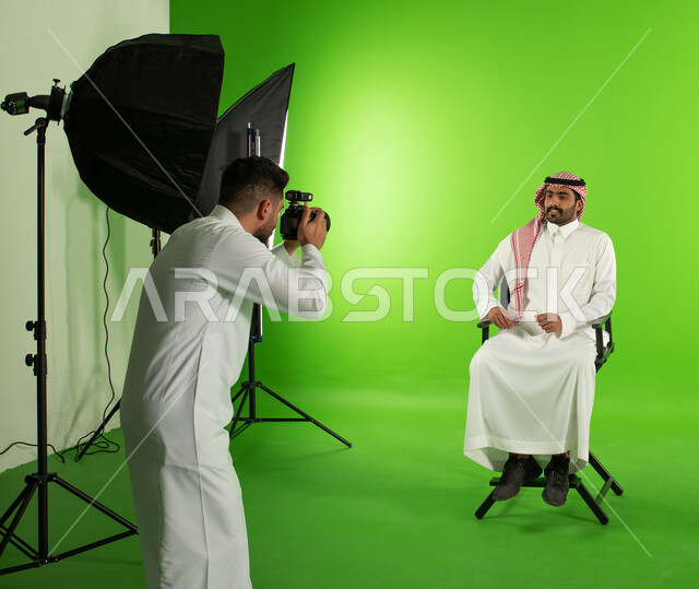 كروما لجلسة تصوير في الاستوديو، كاميرات ومعدات متطورة، مصور محترف عربي سعودي خليجي يقوم بالتقاط صور فوتوغرافية لرجل يرتدي الزي السعودي التقليدي، تصوير اعلاني تسويقي، خلفية شاشة خضراء، خلف الكواليس
