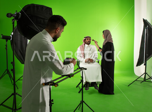 الاستعداد لجلسة التصوير، كروما لجلسة تصوير في الاستوديو، مصور محترف عربي سعودي خليجي يقوم بتجهيز الكاميرا الالكترونية الحديثة، تجميل وتحضير العارض للصور الفوتوغرافية، خلفية شاشة خضراء، خلف الكواليس