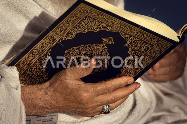 تلاوة وحفظ القرآن الكريم ، صورة مقربة لإيدي رجل مسن عربي خليجي سعودي يحمل بيده المصحف الشريف ، قراءة القرآن الكريم ، إسلاميات وعبادة ،  أذكار في شهر رمضان المبارك, أداء فريضة الحج و العمرة.