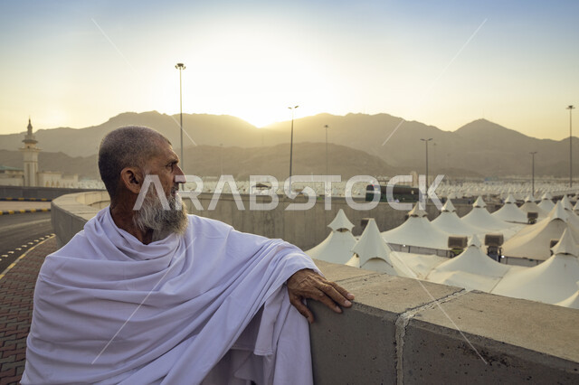 رجل مسن يرتدي ملابس الإحرام يجلس امام المشاعر المقدسه في مكة المكرمة، آداء مناسك الحج ،موسم الحج 2023، اماكن اسلامية مقدسة في المملكة العربية السعودية ، العبادة والتقرب الى الله, خيام و مبيت حجاج بيت الله الحرام في مشعر منى .