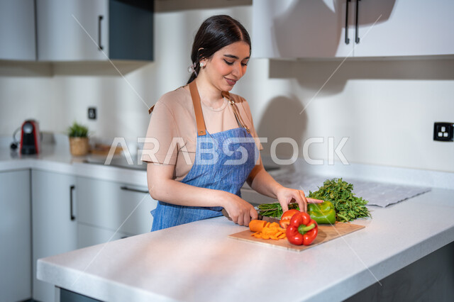 ايماءات تدل على السعادة, ربة منزل عربية خليجية سعودية في المطبخ, ارتداء المئزر و تقطيع الخضار , مفهوم النظام الغذائي، غذاء صحي ومفيد، سلطة الخضار الطازجة اللذيذة، إعداد و تحضير الطعام، وصفات الطعام الشهية