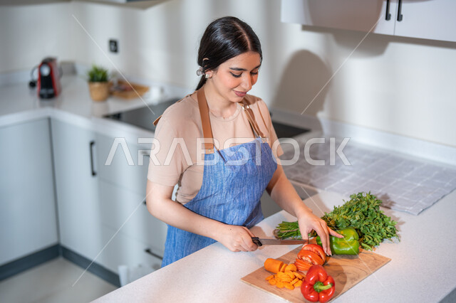 سلطة الخضار الطازجة اللذيذة، ربة منزل عربية خليجية سعودية مبتسمة في المطبخ, ارتداء المئزر و تقطيع الخضار , مفهوم النظام الغذائي، غذاء صحي ومفيد، إعداد و تحضير الطعام، وصفات الطعام الشهية